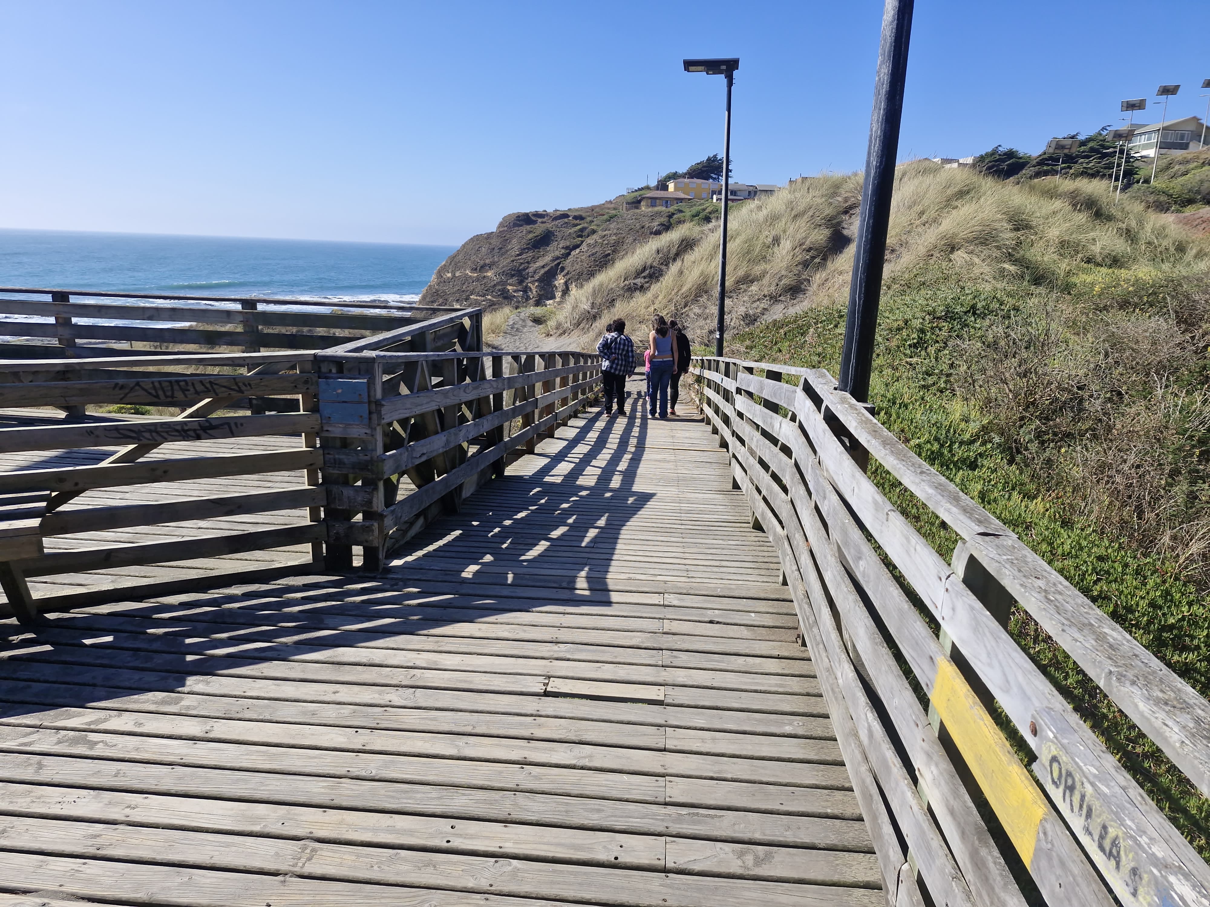 Fotografía del sendero del mirador, es de madera, cuenta con pendiente en norma y se apecian turistas